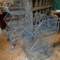 Deux chariots de rangement en fil métallique Casiers d'épicerie Caddie 1970, chacun doté de trois étagères, sont posés sur un sol en bois dans un charmant décor de boutique vintage. Brocante 93