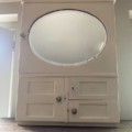 L'Armoire murale 1950 est une armoire murale en bois blanc avec un miroir ovale et deux petits tiroirs - parfaite pour ajouter un charme vintage à n'importe quelle pièce. Brocante 93