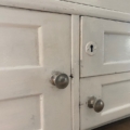Gros plan sur deux portes en bois blanc de l'Armoire murale 1950, avec des boutons ronds argentés et un trou de serrure. Brocante 93