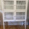 Le Garde manger vintage 1950 est un meuble en métal blanc doté de portes grillagées et de pieds, qui évoque le style classique des années 1950 ; il est présenté sur un sol en bois, devant un mur de couleur claire. Brocante 93