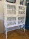 Le garde-manger vintage de 1950, une grande cage à oiseaux en métal blanc à quatre compartiments, se détache sur un mur bleu et blanc, posé sur un sol en bois. Brocante 93