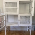 La « Garde manger vintage 1950 », une cage à oiseaux en métal blanc dotée de trois portes ouvertes, trône sur un sol en bois devant un mur clair, apportant une touche du charme des années 1950 à votre intérieur. Brocante 93