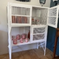Le « Garde manger vintage 1950 » est un meuble de cuisine des années 1950 contenant des bocaux et des bouteilles, posé sur un parquet contre un mur. Brocante 93