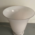 La lampe Art déco en opaline de 1930, caractérisée par son verre opaline blanc évasé, repose sur un socle gris, son cordon d'alimentation étant visible à gauche, et incarne l'élégance raffinée et le charme du style Art déco des années 1930. Brocante 93