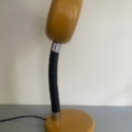 Une lampe berlinoise vintage jaune datant de 1970, dotée d'un col noir flexible, trône sur une surface grise devant un mur blanc, évoquant le charme intemporel du design classique des années 1970 et apportant une touche rétro élégante à n'importe quel espace. Brocante 93