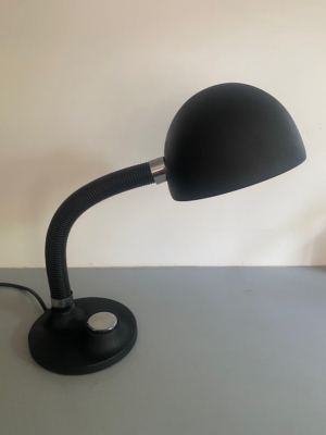 Lampe berlinoise de 1970 — cette élégante lampe de bureau noire, dotée d'un bras flexible, d'un abat-jour en forme de dôme et d'un socle rond, repose sur un support gris clair et incarne l'essence même du design du milieu du siècle, rappelant les luminaires emblématiques des années 1970. Brocante 93