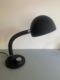 Lampe berlinoise de 1970 — cette élégante lampe de bureau noire, dotée d'un bras flexible, d'un abat-jour en forme de dôme et d'un socle rond, repose sur un support gris clair et incarne l'essence même du design du milieu du siècle, rappelant les luminaires emblématiques des années 1970. Brocante 93