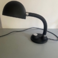 La lampe berlinoise de 1970, avec son col flexible et son socle rond, repose sur une surface grise devant un mur uni ; ses lignes épurées apportent une subtile touche vintage. Brocante 93