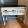Un « Meuble de dentiste 1950 », une armoire vintage en métal dotée de six tiroirs et de roulettes, est placée dans un coin d'une pièce au sol en parquet. Brocante 93
