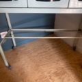 Le « Meuble de dentiste 1950 » est une table en métal bleu clair dotée de tiroirs et équipée de roulettes, photographiée devant un mur bleu et blanc, posée sur un sol en contreplaqué. Ce mobilier dentaire vintage apporte un charme classique et un style fonctionnel à n'importe quel espace. Brocante 93
