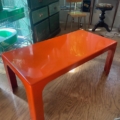 Une table basse orange vif datant des années 1970 posée sur un parquet, avec en arrière-plan des meubles vintage des années 1970. Brocante 93