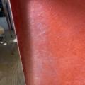 Gros plan sur une chaise en plastique rouge rayée datant des années 1970, avec la lumière du soleil qui pénètre dans la pièce et un parquet visible à l'arrière-plan, à côté d'une table basse 1970 aux lignes épurées. Brocante 93