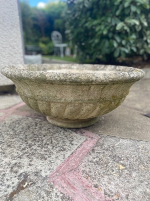 Une vasque en pierre datant de 1960 trône sur une terrasse, avec de la verdure en arrière-plan, floue. Brocante 93