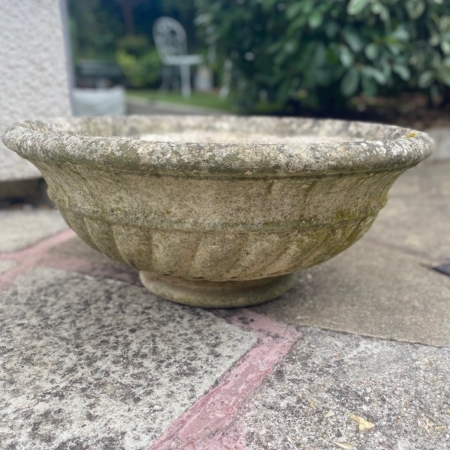 Une vasque en pierre datant de 1960 trône sur une terrasse, avec de la verdure en arrière-plan, floue. Brocante 93