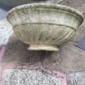 Une grande vasque en pierre datant de 1960, vide, est couchée sur le flanc sur une surface pavée à l'extérieur. Brocante 93