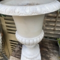 Vase Médicis blanc du XXe siècle posé sur un socle en bois patiné, avec un décor rustique et de la verdure à proximité. Brocante 93