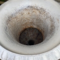 Vase Médicis blanc du XXe siècle, présentant une finition blanche parsemée de taches de rouille et un trou de drainage central, posé sur une surface en bois patinée. Brocante 93