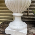 Vase Médicis blanc du XXe siècle : cette urne décorative blanche servant de jardinière, dotée d'une base carrée et posée à l'extérieur sur une surface en bois patiné, évoque l'élégance intemporelle du XXe siècle. Brocante 93