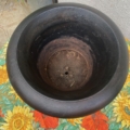 Un vase Médicis du XXe siècle, grand et vide, au fini noir, trône à l'extérieur sur une nappe à motifs de tournesols. Brocante 93