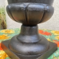 Le « Vase Médicis XXe siècle », une jardinière noire dotée d'une base arrondie et cannelée reposant sur un socle carré, trône avec élégance sur une nappe à motif de tournesols. Brocante 93
