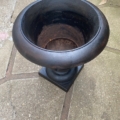 Un grand vase Médicis noir et vide du XXe siècle trône sur une terrasse en pierre ; avec son large rebord arrondi et sa base carrée, il évoque l'élégance de l'aménagement des jardins du XXe siècle. Brocante 93