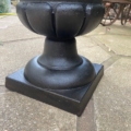 Le « Vase Médicis XXe siècle », une jardinière sur socle noir au design cannelé rappelant les styles classiques, trône sur une terrasse en pierre dont le dallage texturé est bien visible. Brocante 93