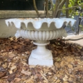 La « Vasque Médicis XXe siècle » — une jardinière décorative blanche au bord festonné — trône, vide, sur du paillis, à l'extérieur, au milieu de branches feuillues. Brocante 93