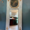 Miroir trumeau du XIXe siècle, orné de détails dorés et d'une scène ovale peinte dans sa partie supérieure, représentant l'intérieur d'une cuisine. Brocante 93