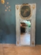 Le miroir trumeau du XIXe siècle, avec son haut cadre ancien et ses touches dorées, se détache sur un mur bleu, entouré de décorations murales, reflétant ainsi le décor éclectique d'une pièce d'inspiration XIXe siècle. Brocante 93