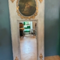 Miroir trumeau du XIXe siècle, orné de détails dorés, d’une peinture dans sa partie supérieure et reflétant des chaises dans son verre. Brocante 93