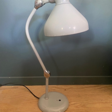 Une lampe de bureau réglable Lampe Jumo GS1 blanche datant de 1950 trône sur un parquet, devant un mur bleu clair, mettant en valeur le design intemporel des années 1950. Brocante 93