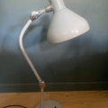 Une lampe Jumo GS1 de 1950 repose sur une surface en bois, devant un mur vert uni. Brocante 93