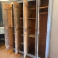 Une armoire en bois datant de 1940, la « Vestiaire en bois 1940 », se dresse, ses trois portes ouvertes dévoilant des étagères et des compartiments vides : ce meuble vintage incarne le charme intemporel d’une époque révolue. Brocante 93