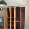 Un vaste vestiaire en bois datant de 1940, doté de nombreux compartiments et de portes ouvertes, trône dans une pièce lumineuse, conférant à l'espace un charme vintage. Brocante 93