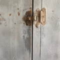 Un loquet métallique rouillé maintient fermées deux portes en bois grises et patinées, présentant des rayures visibles et des éclats de peinture, qui reflètent tout le charme authentique du « Vestiaire en bois 1940 ». Brocante 93