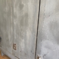 Gros plan sur le « Vestiaire en bois 1940 » : une armoire vintage en bois aux charnières apparentes et à la peinture grise usée, qui dégage tout le charme intemporel d'un meuble des années 1940. Brocante 93
