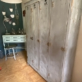 Une pièce chaleureuse mettant en valeur le « Vestiaire en bois 1940 » — un casier en bois gris portant les numéros 1 à 4 —, associé à un petit bureau vert, un tabouret et des décorations murales, créant ainsi un espace accueillant qui respire le charme des meubles vintage, pour tous ceux qui apprécient le cachet d'un vestiaire des années 1940. Brocante 93