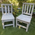 Deux chaises en bois patinées, la « Paire de chaises enfant 1950 », sont posées sur l'herbe verte, avec des buissons feuillus en arrière-plan. Brocante 93