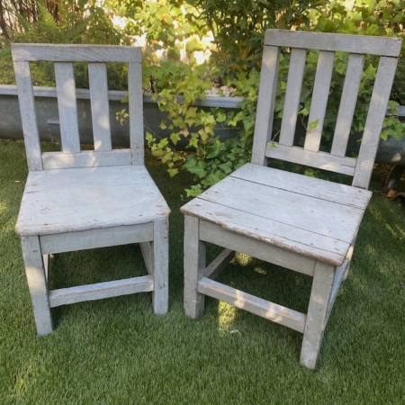 Deux chaises en bois patinées, la « Paire de chaises enfant 1950 », sont posées sur l'herbe verte, avec des buissons feuillus en arrière-plan. Brocante 93
