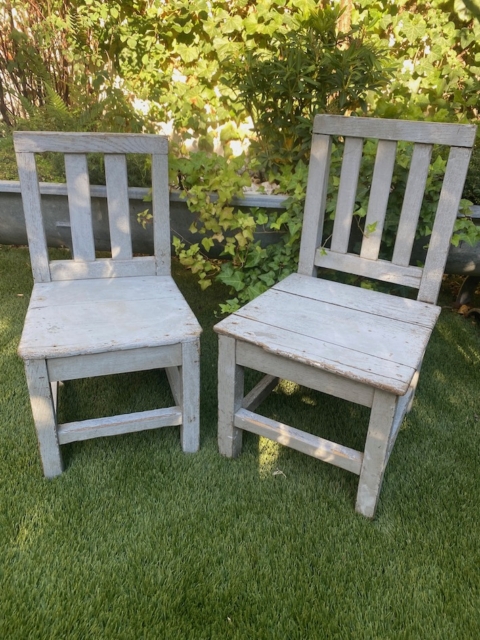 Deux chaises en bois patinées, la « Paire de chaises enfant 1950 », sont posées sur l'herbe verte, avec des buissons feuillus en arrière-plan. Brocante 93