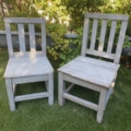 Une paire de chaises pour enfants datant des années 1950 est posée sur l'herbe verte, avec en toile de fond des buissons feuillus. Brocante 93