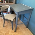 Un bureau d'enfant et une chaise des années 1960, posés sur un parquet clair devant un mur bleu, qui dégagent un charme rétro. Brocante 93