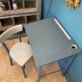 Un « Bureau d’enfant & chaise 1960 » compact, de couleur gris vintage, trône sur un parquet, près d’un mur bleu et d’étagères, incarnant tout le charme nostalgique du design du milieu du siècle dernier. Brocante 93
