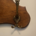 Le « Porte-serviettes 1960 », un porte-manteau en laiton inspiré du design du milieu du siècle, est fixé sur une plaque en bois posée contre un mur de couleur claire, projetant une ombre délicate. Brocante 93