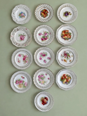 Treize assiettes à dessert de 1950, avec des bords ajourés et des motifs floraux ou fruités. Brocante 93