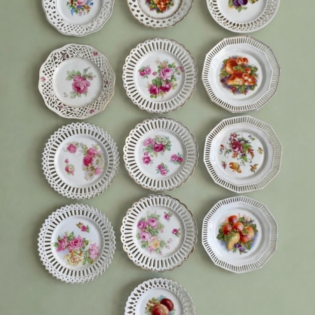 Treize assiettes à dessert de 1950, avec des bords ajourés et des motifs floraux ou fruités. Brocante 93