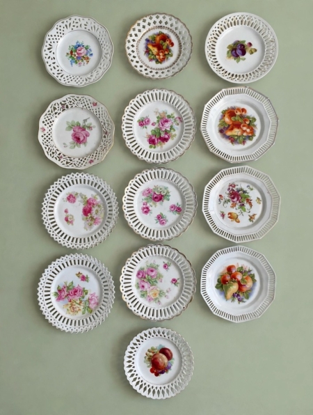 Treize assiettes à dessert de 1950, avec des bords ajourés et des motifs floraux ou fruités. Brocante 93