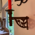 Une bougie rouge dans une applique décorative en laiton « Chandelier de piano 1960 », fixée près d'une fenêtre et de miroirs. Brocante 93