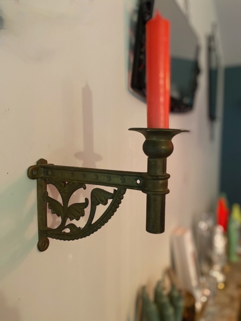Le « Chandelier de piano 1960 » se compose d'une applique métallique ouvragée surmontée d'une grande bougie rouge, qui lui confère une élégance vintage. Brocante 93
