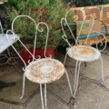 Deux chaises en fer forgé des années 1950, présentant des traces de rouille et dotées de dossiers ouvragés en volutes, disposées sur une terrasse en pierre. Brocante 93